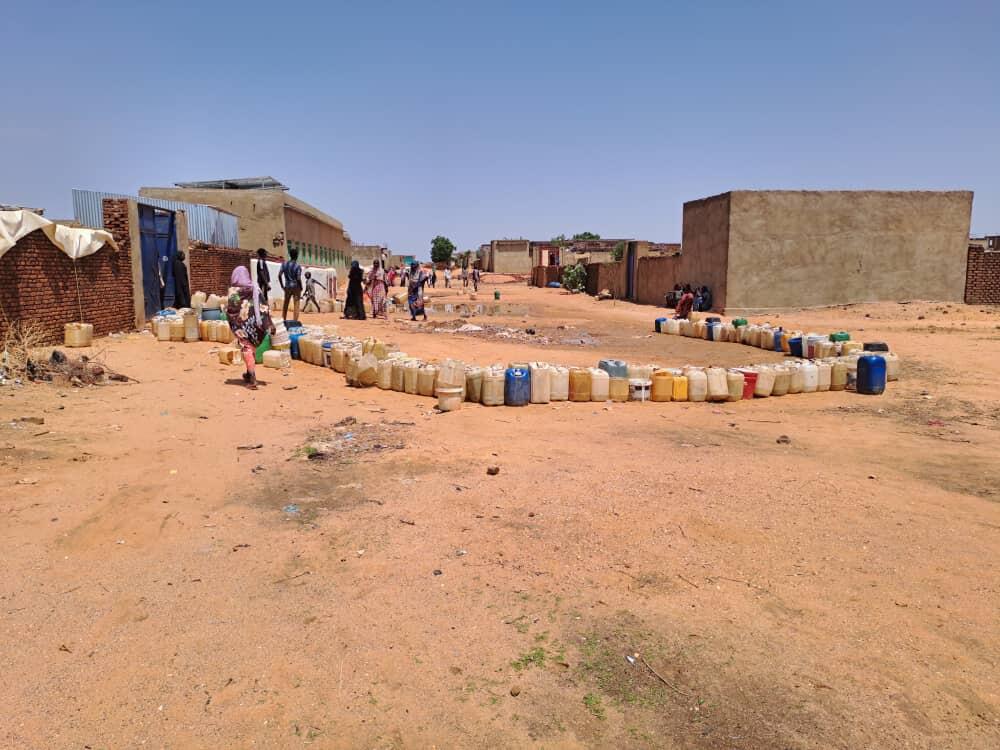 People cautiously keep a distance as their jerrycans wait in line at one of the few accessible water points - Sudan