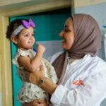 En MSF-sundhedsmedarbejder holder den lille pige Zahraa under et opfølgningsbesøg for TB-behandling på Al-Mahdi Health Center i Sadr City, Bagdad, som led i indsatsen for tidlig screening og oplysning om tuberkulose.