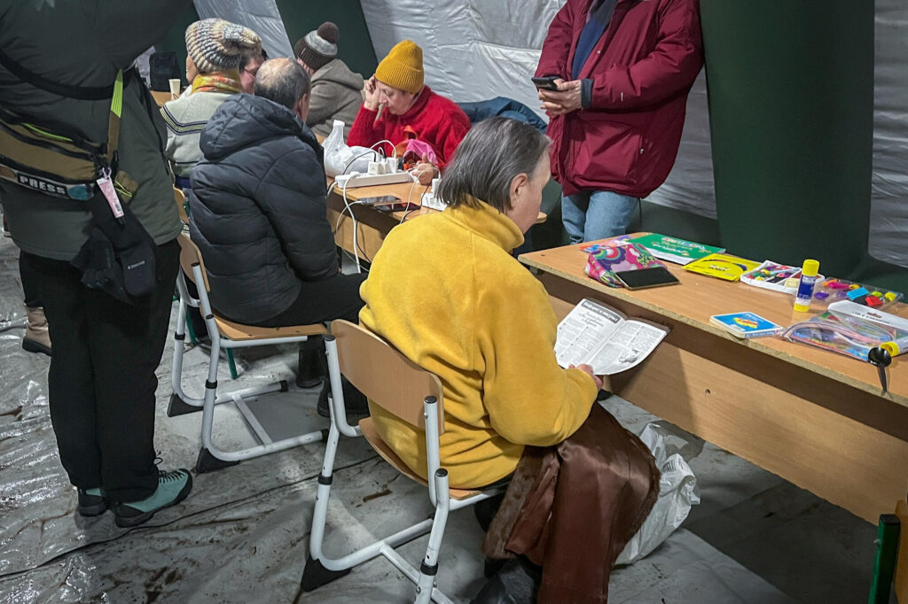 People warm up and wait for their devices to charge inside an emergency tent in Kyiv - Ukraine