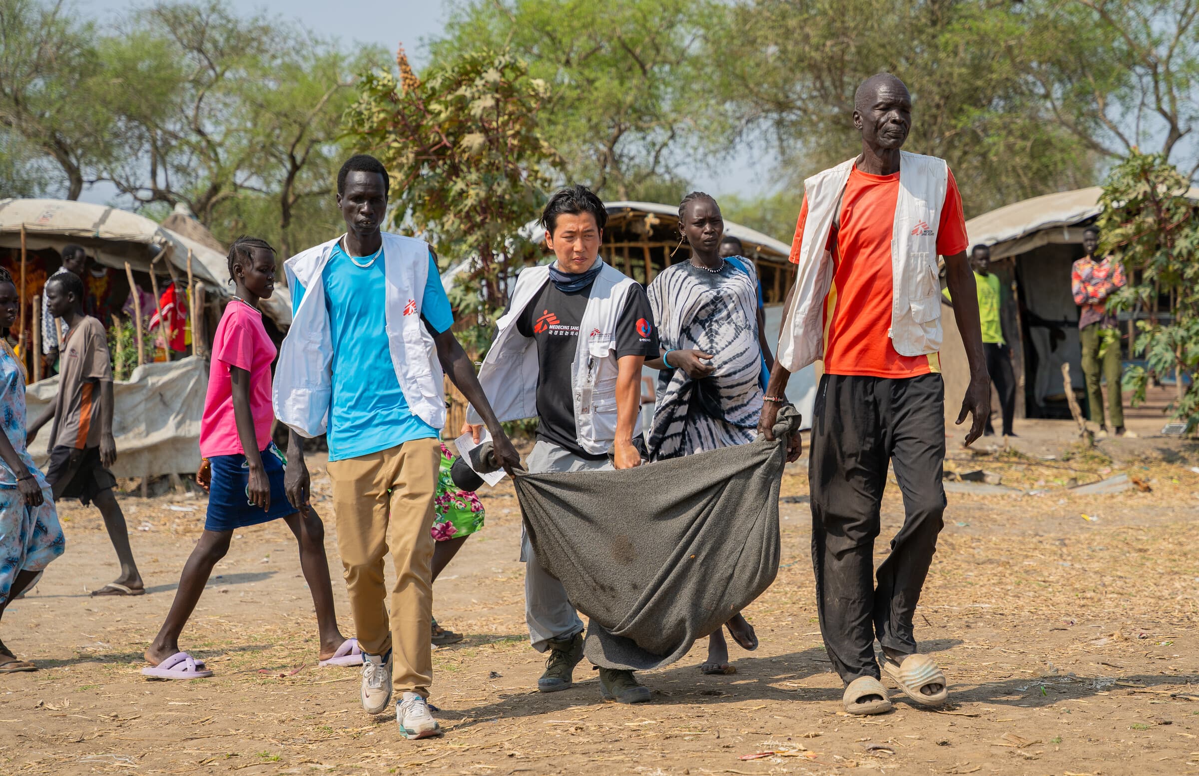 Marts. Sydsudan. Vores medarbejdere bærer en alvorligt såret patient mod båden, der skal transportere ham fra Yakuach til Chuil, Jonglei-delstaten, hvor han kan få yderligere behandling. 